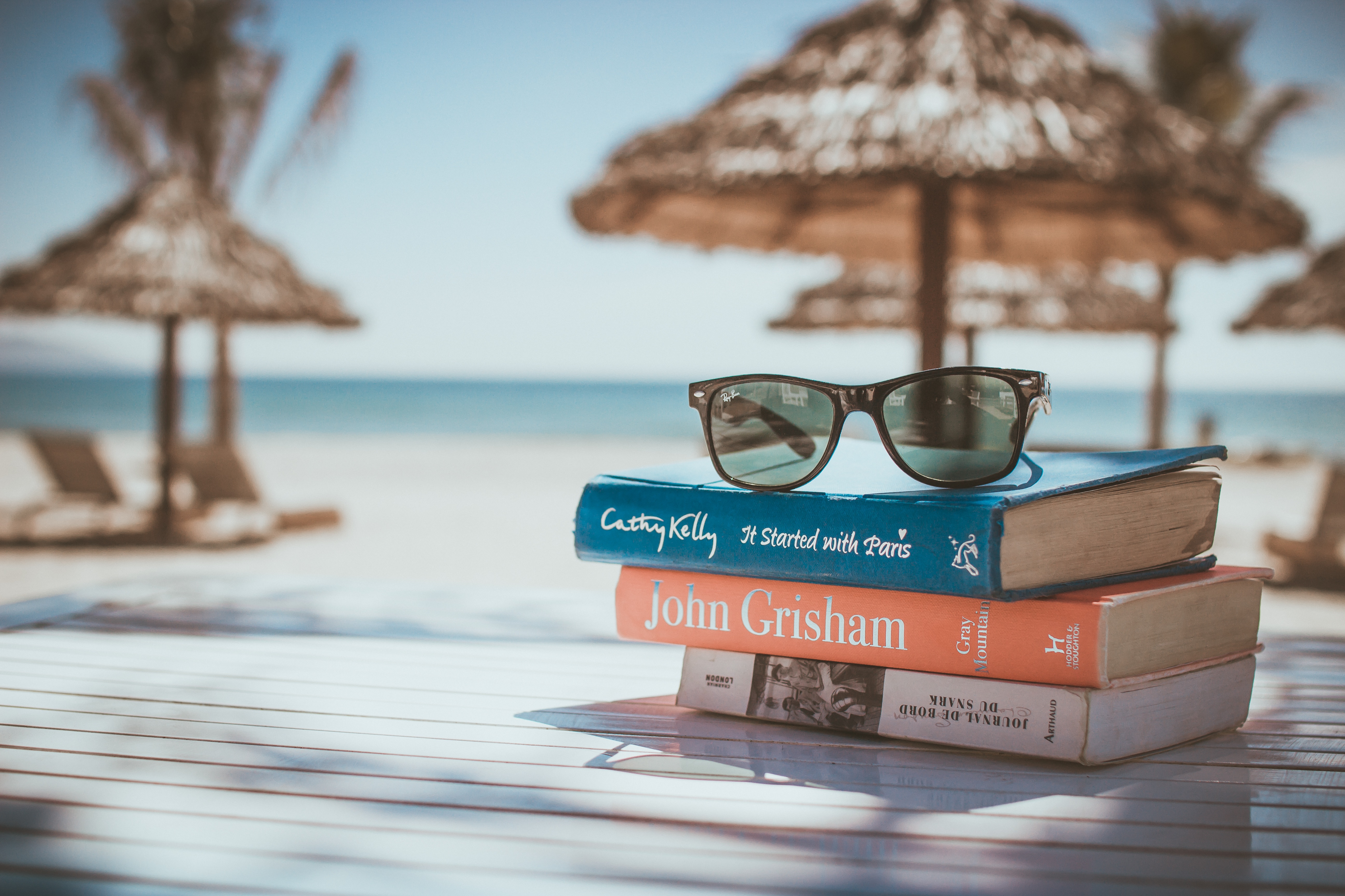 stack of books with sunglasses on top on a beach