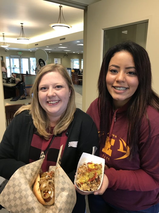 Two WRCU employees eating a Housewife Hotdogs wearing Hornets jersey for Battle of the Bridge