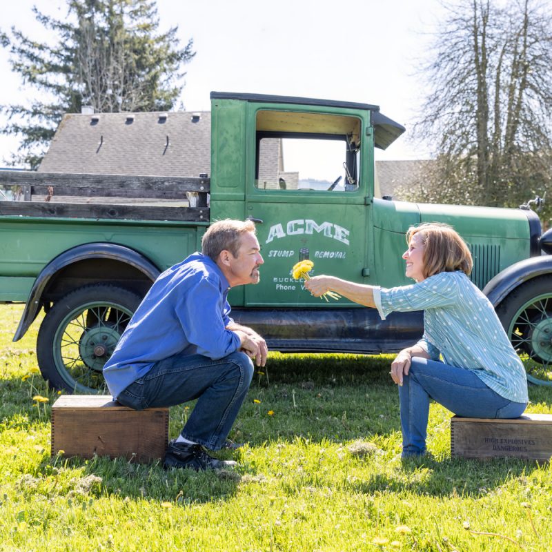 a couple sitting in front of an old green truck smelling flowers and laughing on a blog about saving and spending