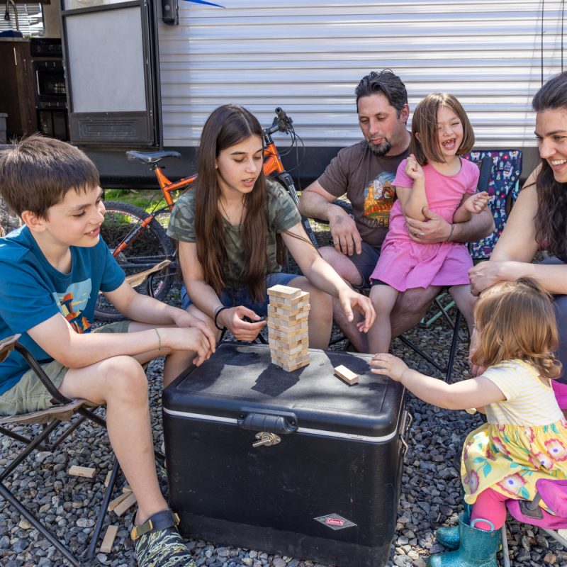 A family playing jenga in front of their RV and discussing back-to-school budget